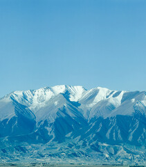 Fototapeta premium Majestic snow-capped Altai Mountains under a bright blue sky with clouds in Xinjiang, China.
