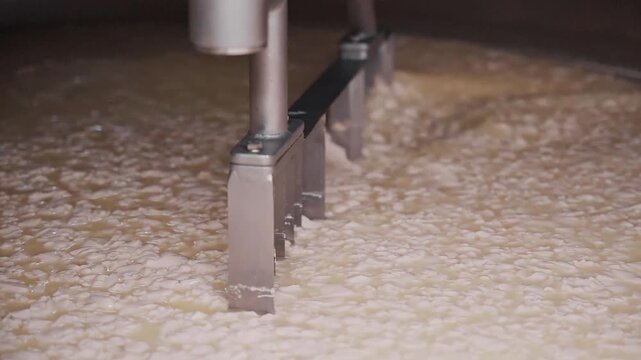 4k close up footage of mechanic arms mixing hot milk at the dairy factory. closeup of wire frames rotating in automated heating vat at cheese plant, cutting yellow mass into pieces and separating it f