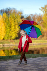 Obraz premium Cute little girl holding colorful rainbow umbrella on beautiful autumn day. Happy child playing in autumn park. Outdoor fun by any weather