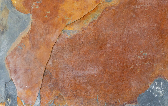 Natural rusty slate stone texture background with orange, brown, and grey colors. Top view full frame of rough mineral flagstone surface, abstract geological pattern
