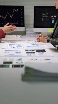 Financial analysts discussing stock market data in a meeting, analyzing financial charts and stock market data on documents and computer screens.