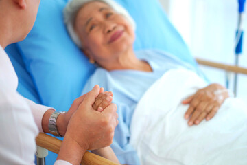 Obraz premium Loving son holding hands with senior mother on hospital bed