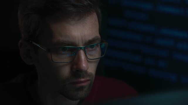 Close-up of a focused coder in eyeglasses, digital programming code reflecting across his lenses in a dark while he deeply engaged in analyzing scripts related to AI or data science. Copy space