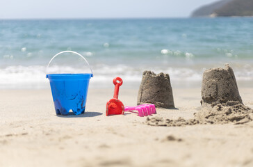 Colorful beach toys and handmade sandcastles on a sunny tropical beach with ocean waves in the background during summer vacation. © Leonardo