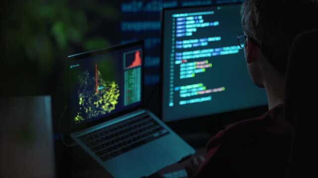 Thoughtful programmer in glasses stares at multiple glowing screens in a dark office. Developer typing code, working through a complex computer science or data science task late at night.