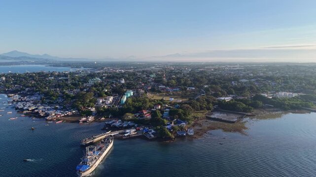 Aerial sunrise view of Puerto Princesa coastal city and calm harbor in Palawan with boats shoreline trees tidal flats and distant mountains