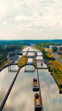 Vertical video. Ghent, Belgium. Sluis Merelbeke, massive steel lock gates and concrete chambers of the Ringvaart bypass canal, aerial forward flight under overcast summer sky. Drone footage. Rich col