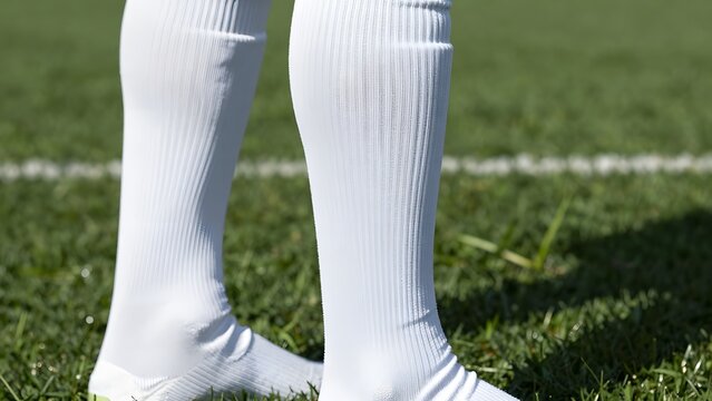 59. [STYLE] of close-up on modern football socks and shin guard sleeve showing gear with tight elastic knit weave, sleek inner guard contour, low-angle side morning sun, crisp white socks and deep eme