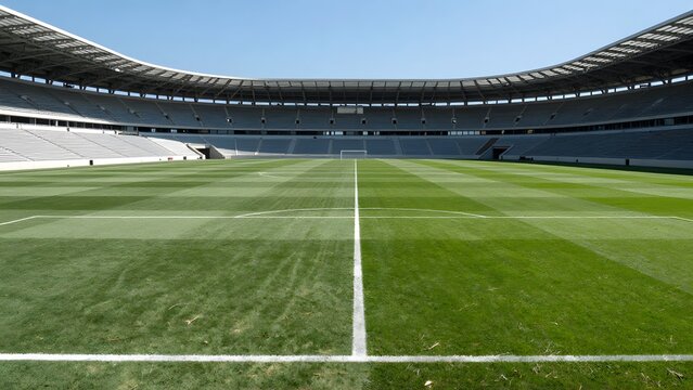 135. [STYLE] of football pitch central circle kickoff view showing scale with vast turf dimensions, white center line, bright midday sun, deep emerald stripes and clear sky blue, monumental stadium bo