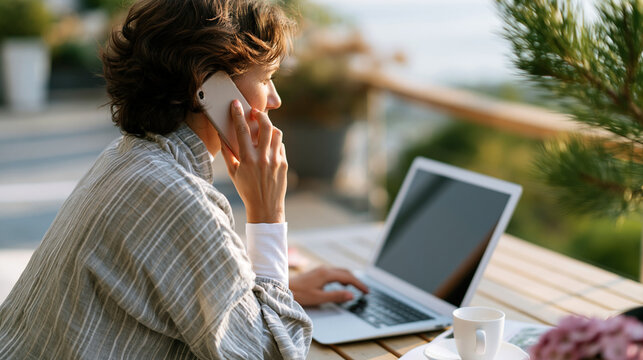 A European woman viewed from behind talks on a soft phone checking a bright laptop on a calm home terrace in soft daylight terrace call faceless back view bright home daylight