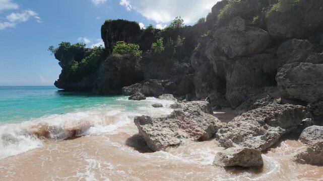 Balangan beach in Uluwatu, Bali. Turquoise deep blue waves crash dramatically on the rocks and shoreline in slow motion on a beautiful sunny clear day, 