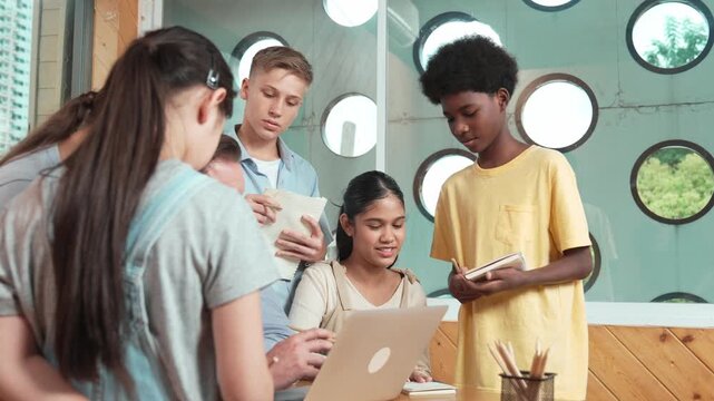 Caucasian teacher giving comment or advise student while smart bot pointing at laptop screen at classroom. Diverse student taking a note while teacher teach lesson while using computer. Edification