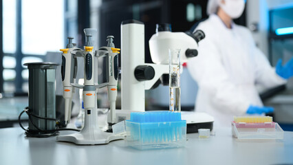 Scientific Laboratory Workbench with Micropipettes, Microscope, and Test Equipment with Researcher in Background © Prathankarnpap