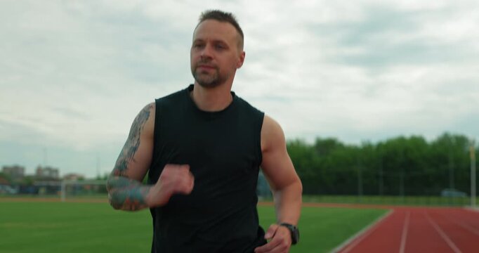 Steadicam front shot of fit sportsman jogging at the athletics arena