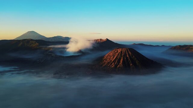 Spectacular drone flyover of active Mount Bromo caldera &ndash; Amazing volcanic dust and sulfur smoke rising in warm golden hour light, premium Indonesia tourism and travel advertising background