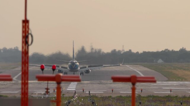 A commercial passenger jet airplane rolling on the runway after landing in Almaty, Kazakhstan. View from behind showing deployed thrust reversers, raised wing spoilers, and strong engine heat haze.