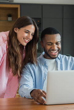 Young adult couple smiling and laughing while looking at a laptop computer together at home, enjoying shared screen time and a modern digital lifestyle