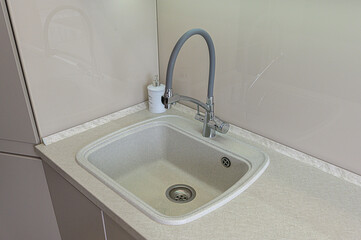Fototapeta premium beige granite-style kitchen sink is embedded in matching countertop; equipped with chrome faucet featuring grey flexible gooseneck spout, a soap dispenser is placed nearby