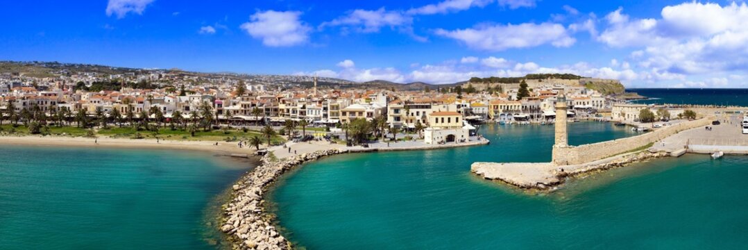Rethymno Crete Greece  aerial drone 18k panorama of Venetian lighthouse. Old town skyline with pink domes church and mosque minaret in background. Historical architecture of Rethymnon harbor