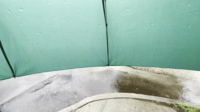 under a green umbrella in a rain storm with runoff water rushing by on the street