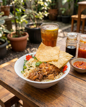 Authentic Indonesian Bakmi Ayam Street Food with Sambal and Iced Tea on Warm Wooden Table in Casual Street Food Setting