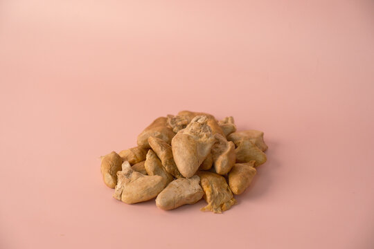 A small pile of premium freeze-dried chicken heart pet treats on a solid pastel pink background. Healthy, natural dehydrated meat dog and cat food. Minimalist studio shot with ample copy space.
