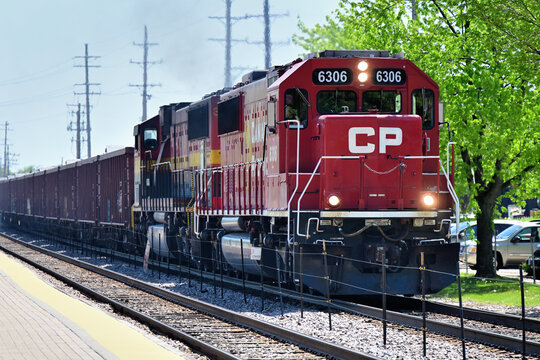 A Canadian Pacific Railway locomoitve leads a Canadian Pacific Kansas City freight train westbound through a Chicago suburb after departing CPKC's Bensenville Yard.
