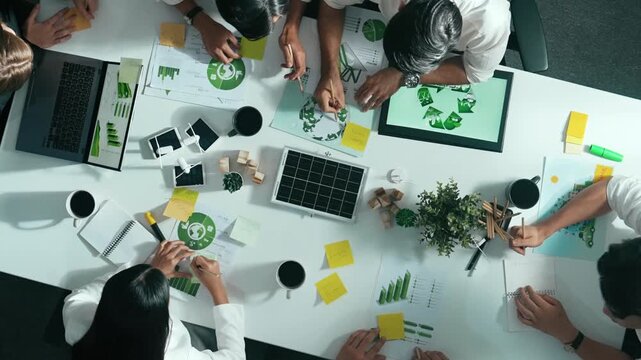 Top down view of business team discussing about using clean energy and sustainable investment at meeting table with wind mill, document with environmental graph and wooden house model. Alimentation.