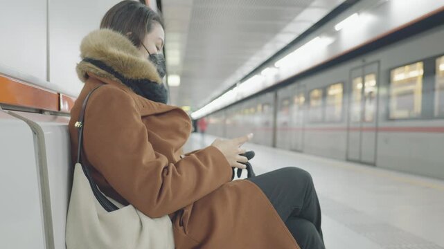 A person seated on a subway bench, absorbed in their mobile device, surrounded by the modern subway environment. The scene captures the essence of daily commuting and urban life.