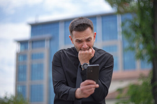 Anxious businessman biting fingers in panic looking at smartphone with copy space