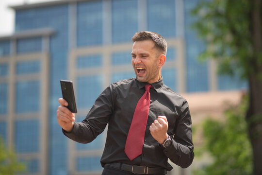 Triumphant businessman celebrating success looking at smartphone with copy space