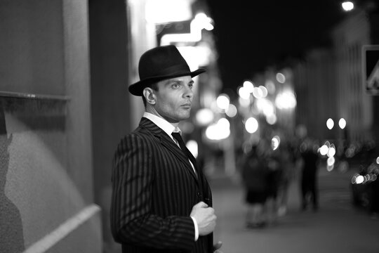 Elegant detective in pinstripe suit and fedora hat on night city street with copy space