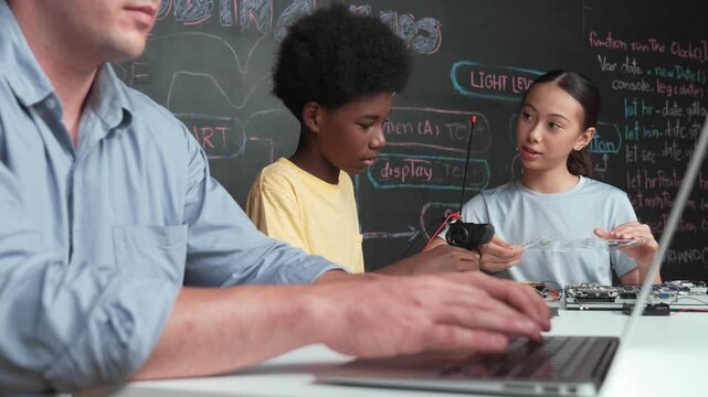 Young student fixing controller while teacher programming engineering code at STEM class. Closeup of instructor hand typing computer while smart girl using electronic tool and blackboard. Edification