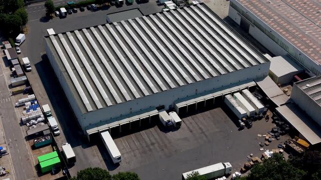 Industrial Warehouse and Logistics: Aerial view of a large industrial warehouse complex with loading docks, trucks, and trailers, signifying logistics and distribution operations.