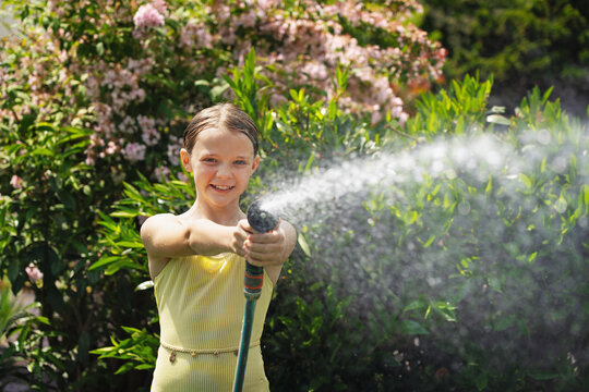 A cheerful child plays with water sprinklers in the garden during the summer. Creatively watering the garden&mdash;with fun and high spirits. An authentic, real little girl.