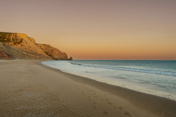 Golden hour sunset over the Atlantic Ocean shoreline with rolling hills, warm light reflecting on the water and a scenic coastal landscape. © Vaidile