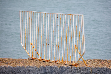 Fototapeta premium Weathered metal barrier rests on rocky shoreline