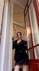 Obraz premium Elegant woman posing in doorway. Fashionable lady wearing black blazer and glove stands in interior. Stylish portrait of woman in classic outfit. Concept of luxury and style.