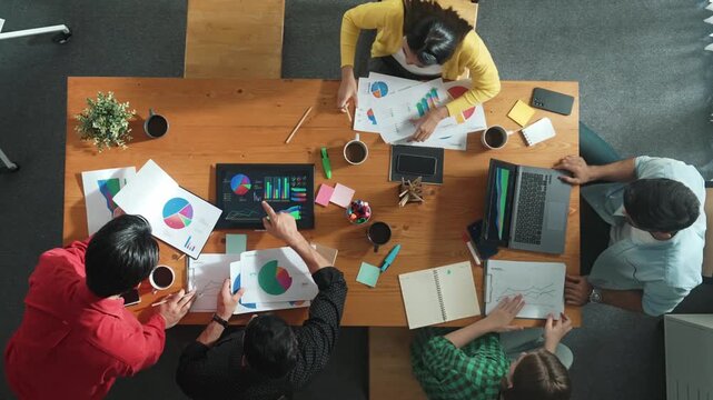 Top view of skilled businessman present marketing idea at meeting while group of investor listening and planning strategy while looking at stock market chart or data analysis document. Convocation.