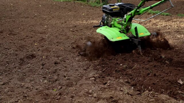 Detailed closeup footage of a young Indian farmer using a power tiller to cultivate fertile farmland in rural Himachal Pradesh during summer season.