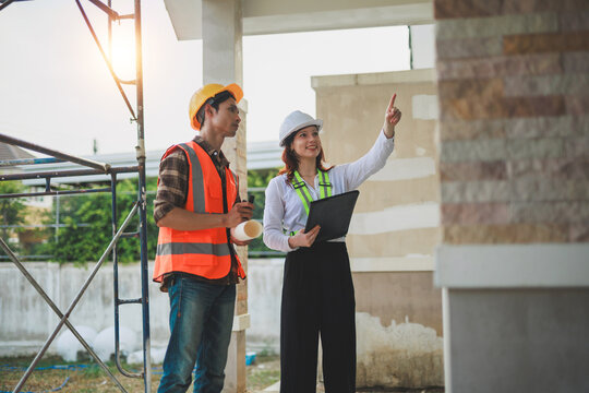 Professional female architect discussing building plans with a male construction worker, wearing safety helmets and vests on site