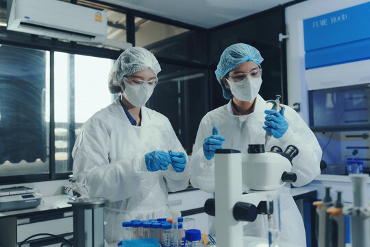 Researchers wearing protective equipment performing experiments and analyzing samples with a microscope in a professional laboratory