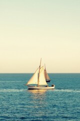 Fototapeta premium Two sailboats glide across calm blue water under a clear sky. The vessels have white sails billowing in the wind. They travel on the ocean horizon.