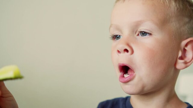 Boy eating a fresh cucumber slice. Cute little boy tasting healthy food and organic vegetables. Kid eating a green cucumber at home. Adorable young kid eating healthy food. 
