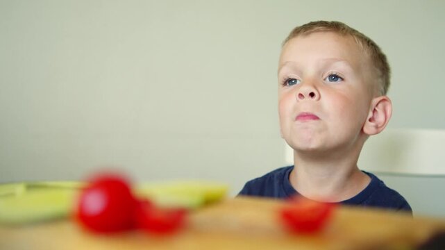 Cute little boy eating fresh vegetable slices. Child tasting healthy food and organic food. Kid eating a red tomato at home. Adorable small kid eating healthy food. 
