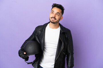Fototapeta premium Young man with a motorcycle helmet isolated on purple background thinking an idea while looking up