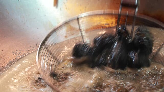 Black tofu frying in hot oil with metal strainer