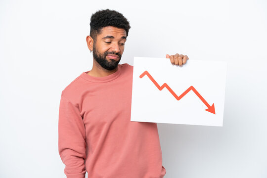 Young Brazilian man isolated on white background holding a sign with a decreasing statistics arrow symbol with sad expression