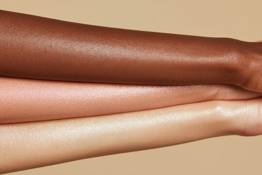 Three diverse women's bare forearms layered together, showcasing varying skin tones against a neutral background, emphasizing diversity and inclusivity in beauty representation