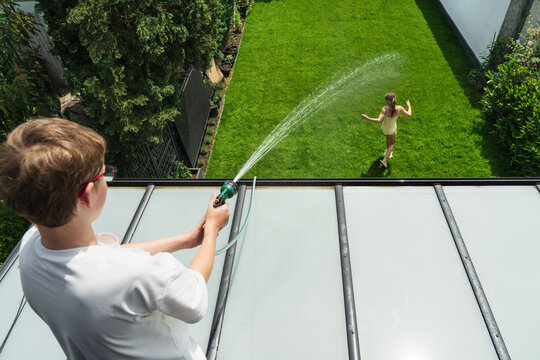 Happy children are playing with water in the garden this summer. A family is playing with a garden hose at home&mdash;full of fun and high spirits.